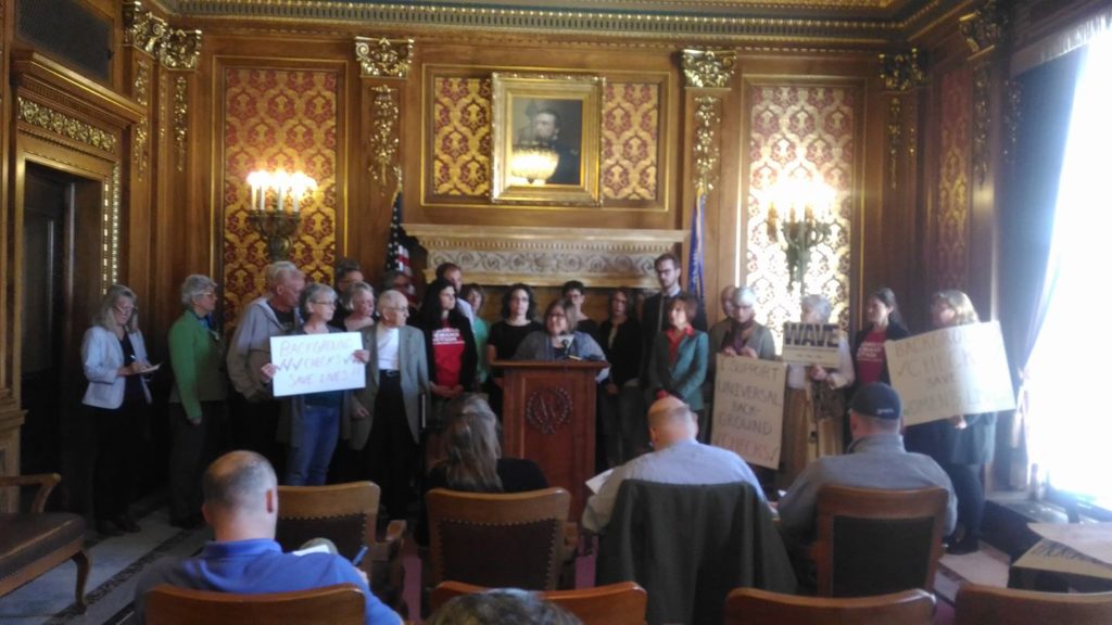 A large group of people are gathered in front of a podium. It is a public event announcing the start of the Wisconsin Gun Safety Coalition.