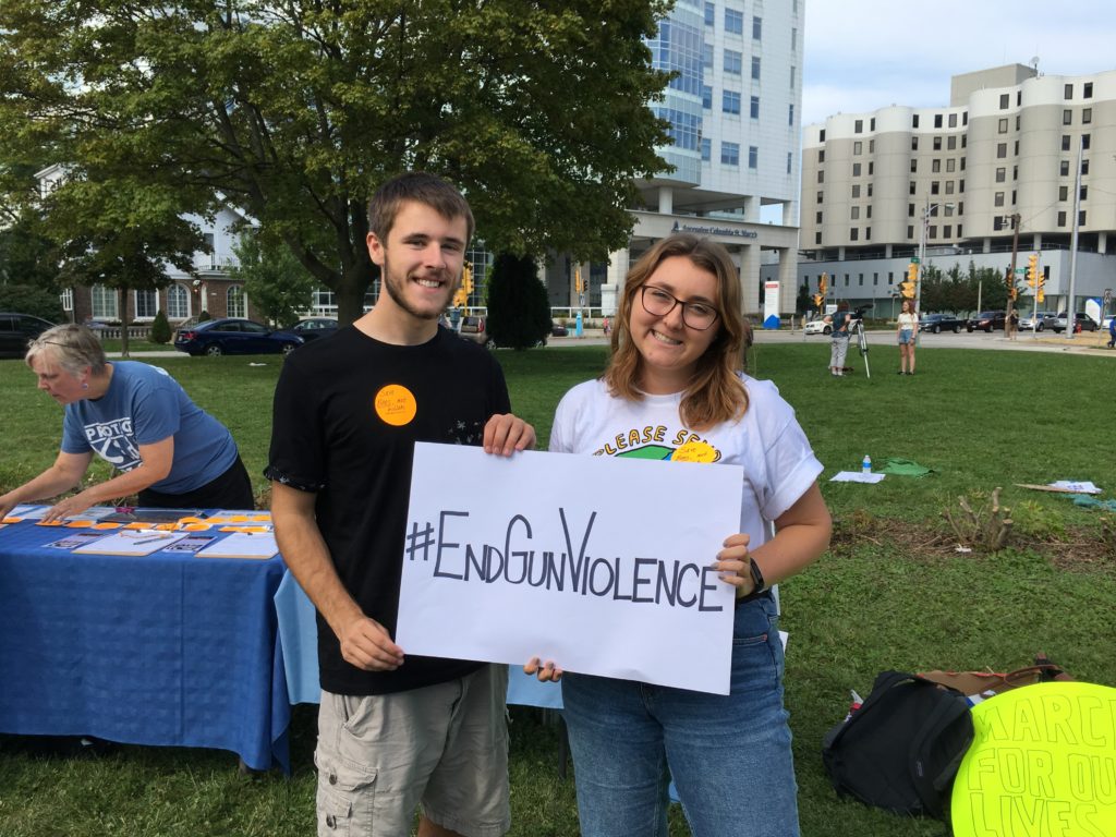Two youth hold a sign at an event. The sign says #EndGunViolence.