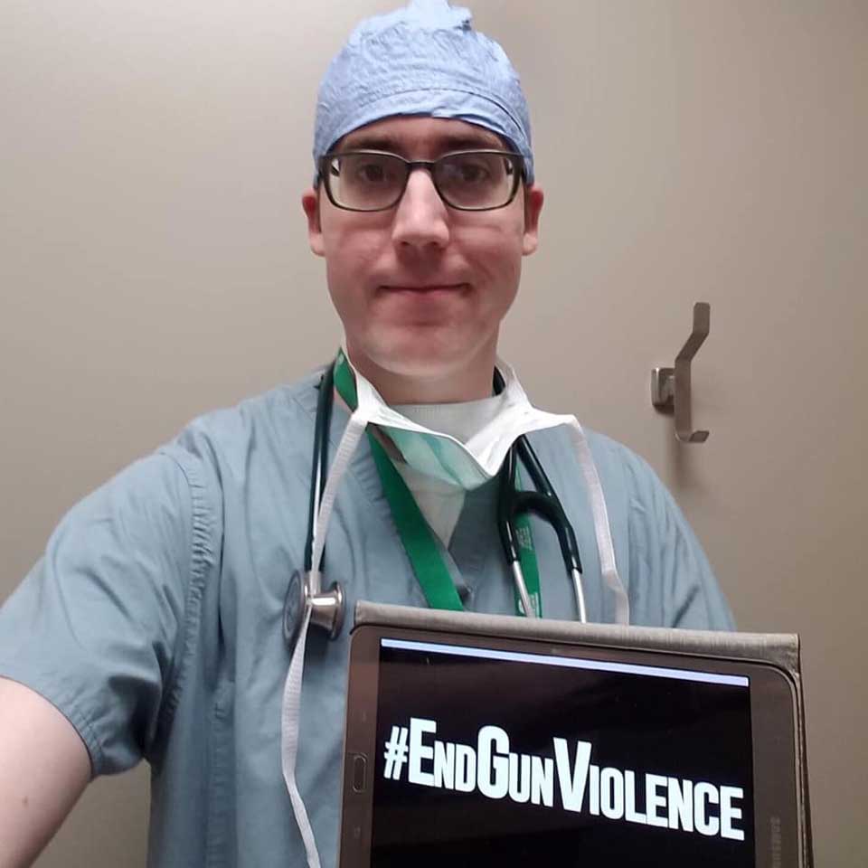Doctor in scrubs holding a sign that says "#End Gun Violence"