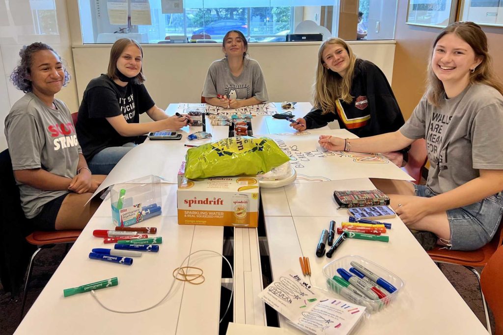 Youth Interns smiling at the camera from around a table filled with sign making supplies