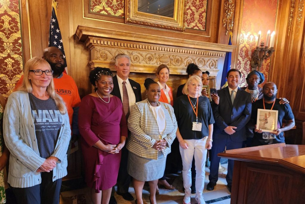 A row of people stands before a podium after a press conference. The people include WAVE's executive director, legislators, and other advocates, including survivors of gun violence.
