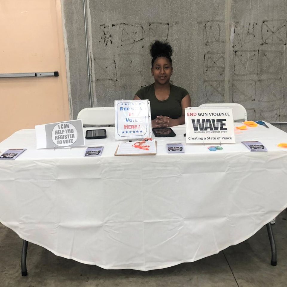 A WAVE youth intern sits at a resource table designed to help people register to vote.