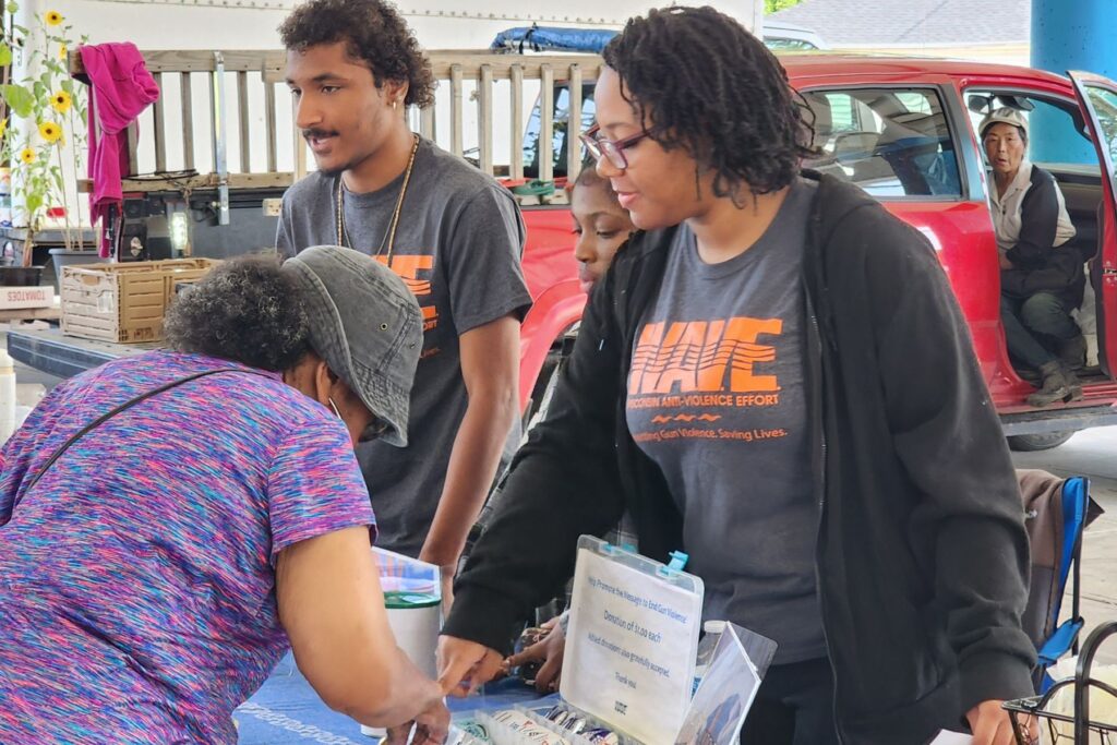 Three WAVE Youth Summer Interns speak with atedees at a farmer's market about gun violence prevention.