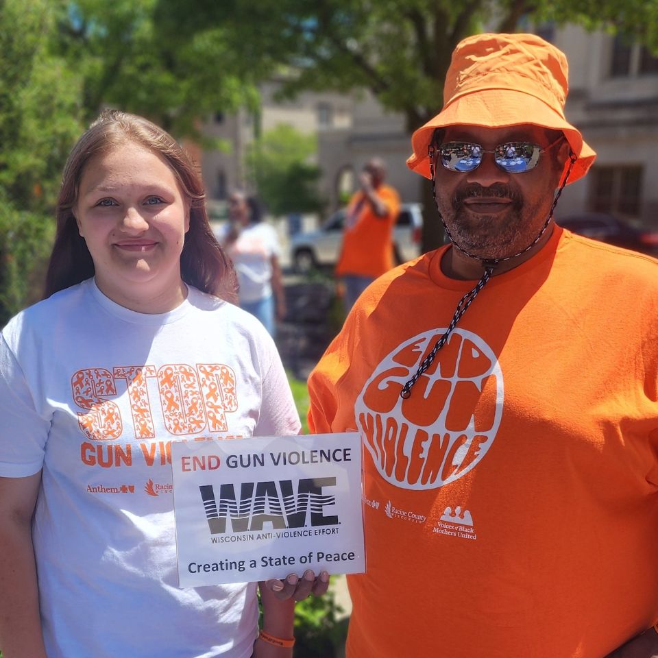 A WAVE Youth member stands with WAVE's Youth Program Manager. They hold a sign that says End Gun Violence.