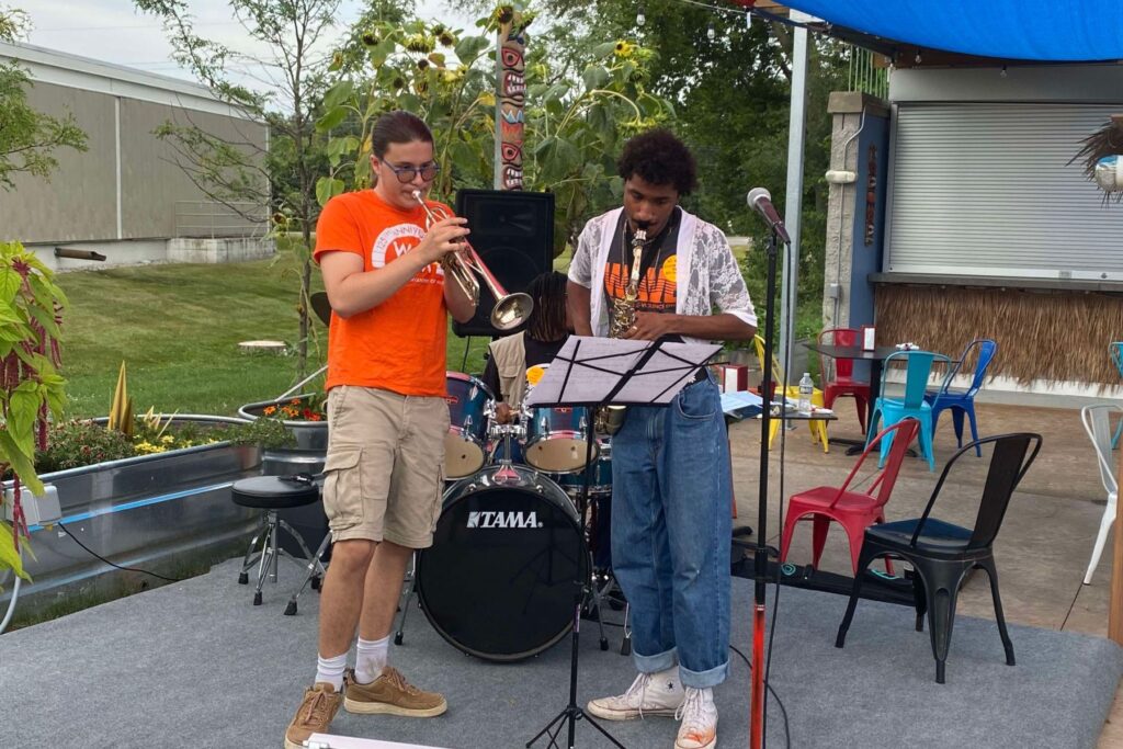 A WAVE Youth Summer Intern plays saxaphone at an event. He is joined by a trumpet player and drummer for a jazz trio.