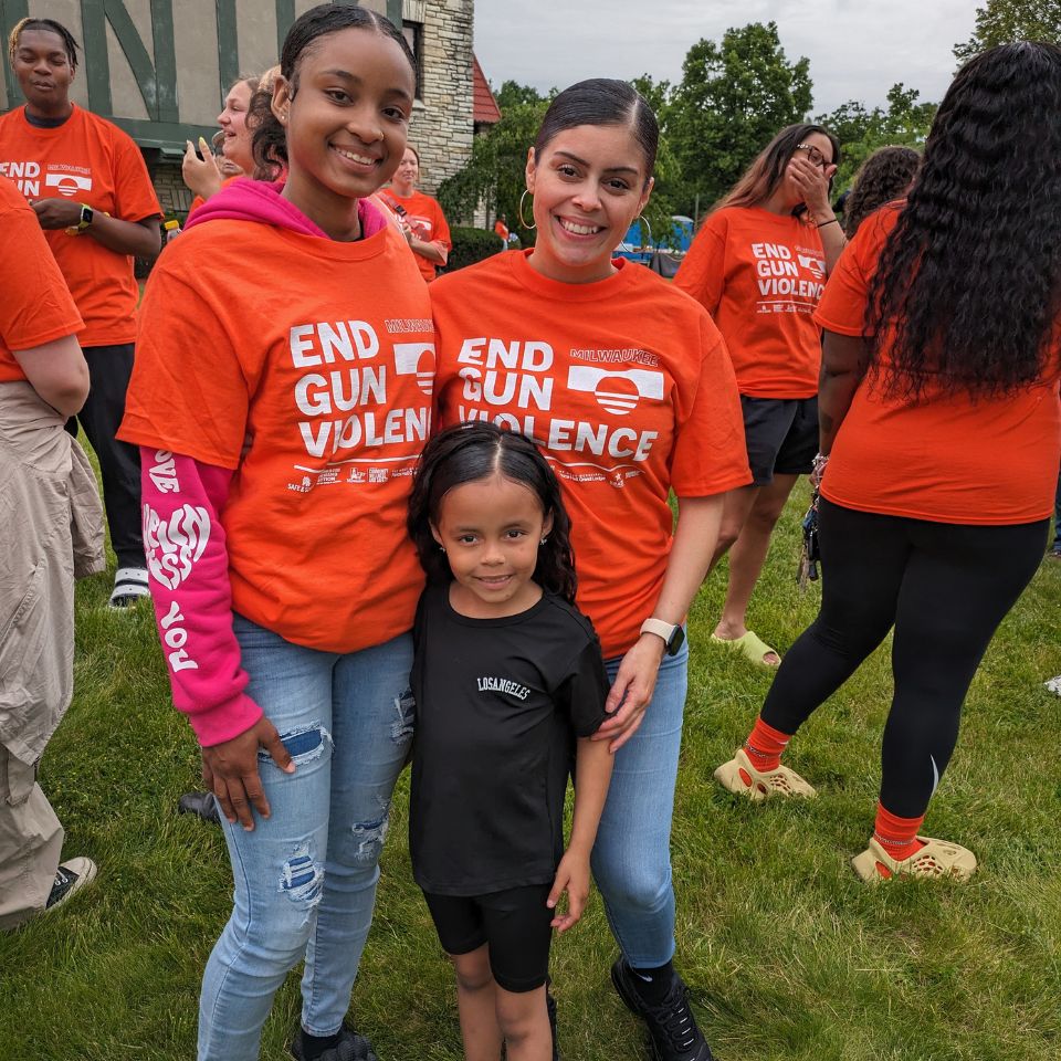 Three people pose together. They appear to be a family - a mother, a teen, and a young child. Their arms are around each other.