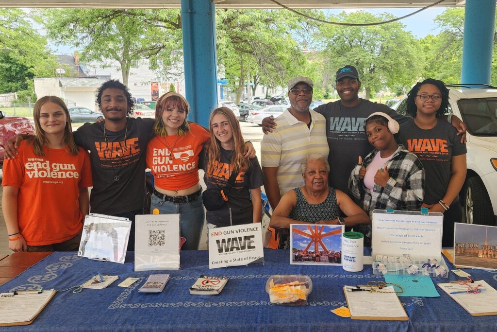 WAVE interns stand behind a table covered in information about gun violence prevention. One intern is joined by family members.