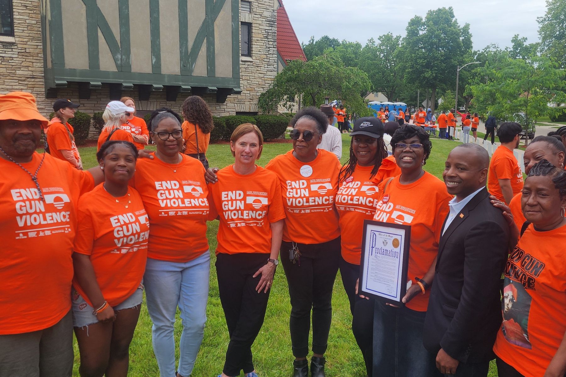 A row of people stands with their arms around each other at Milwaukee's Wear Orange events. It includes WAVE staff, an intern, several partners, survivors, and Milwaukee's mayor.