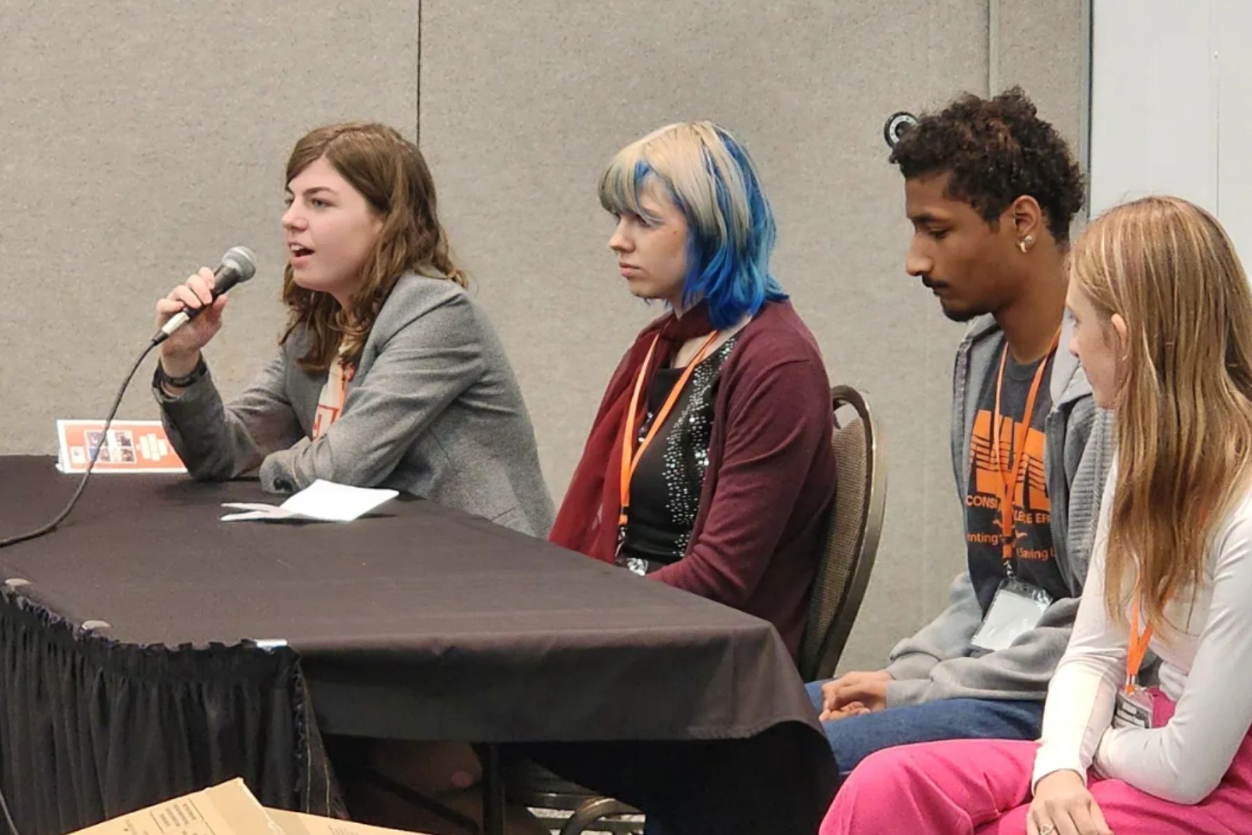 Four youth sit at a table during a panel at the Gun Violence Summit. One is speaking into a microphone 