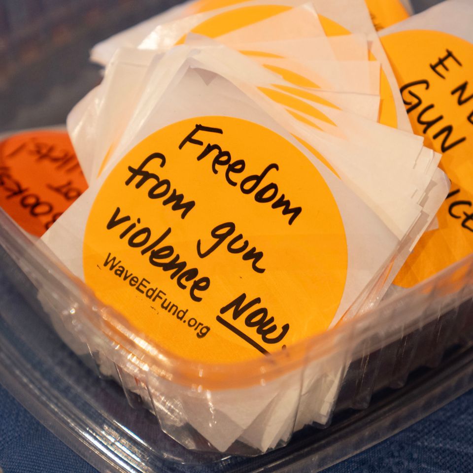 a container of round orange stickers. The top sticker says Freedom from gun violence now!