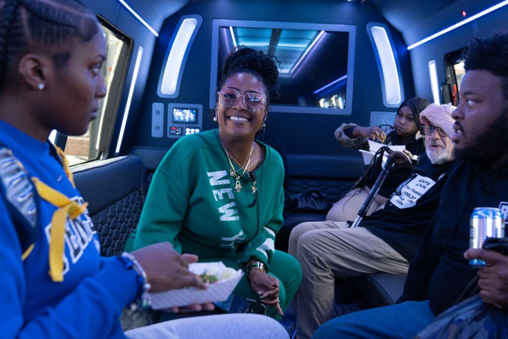 A collection of people sits in a van. The lights are blue, with a party atmosphere. The people are having fun and smiling.