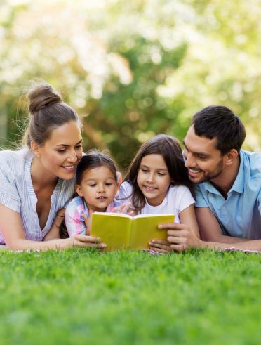 A family lays on the grass, reading a book. The scene is calm and comforting.