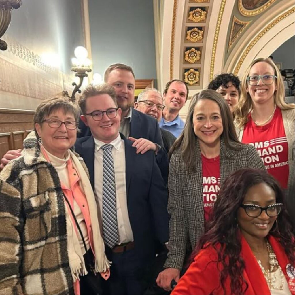 A group of people stand together in a gallery at the Wisconsin Capitol. They all smile with excitement.